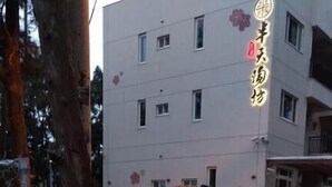 Uma pedra com caracteres chineses e um selo vermelho, localizada em frente a um edifício com várias janelas e entrada protegida por grades.