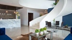A modern hotel lobby with a reception desk, seating area, and a staircase. - Stay Inn Hotels (Reynosa)