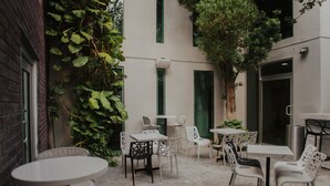 An outdoor patio with white tables and chairs, surrounded by greenery and a brick wall. - Stay Inn Hotels (Reynosa)