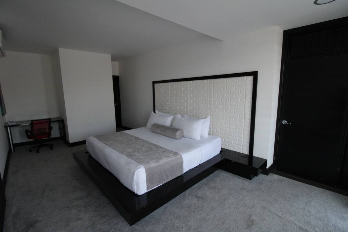 A modern hotel room with a large bed, a desk, and a chair.