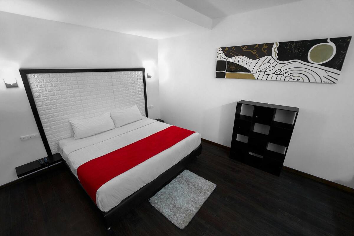 A modern bedroom with a white brick headboard, a red and white bedspread, a gray rug, and a black storage unit.