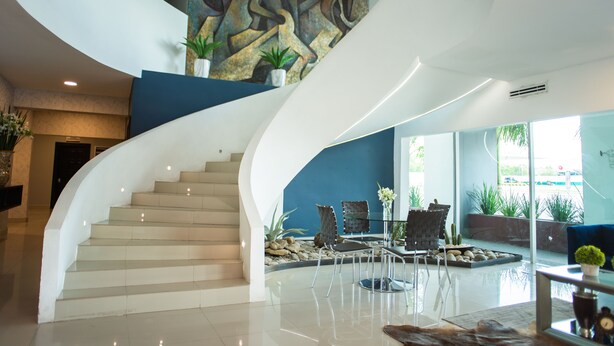 A modern interior with a curved staircase, a blue accent wall, and a seating area with plants. - Stay Inn Hotels (Reynosa)