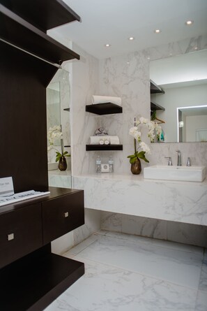 A modern bathroom with a marble countertop, a built-in sink, a vanity with drawers, a mirror, and two vases with white orchids.