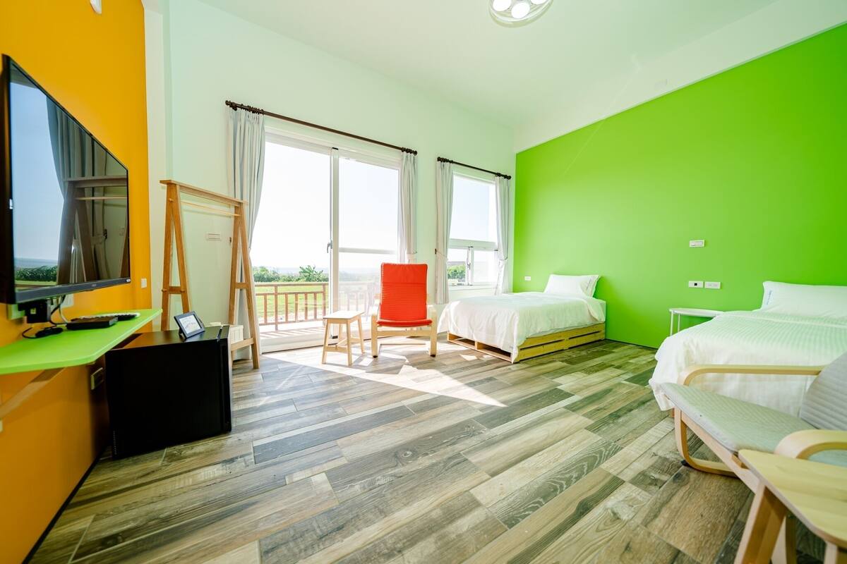 Hotellihuone, jossa on kaksi sänkyä, työpöytä tietokoneella, televisio ja parveke, jolta on näkymä.