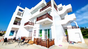 A modern multi-story building with balconies, outdoor seating, and a clear blue sky.