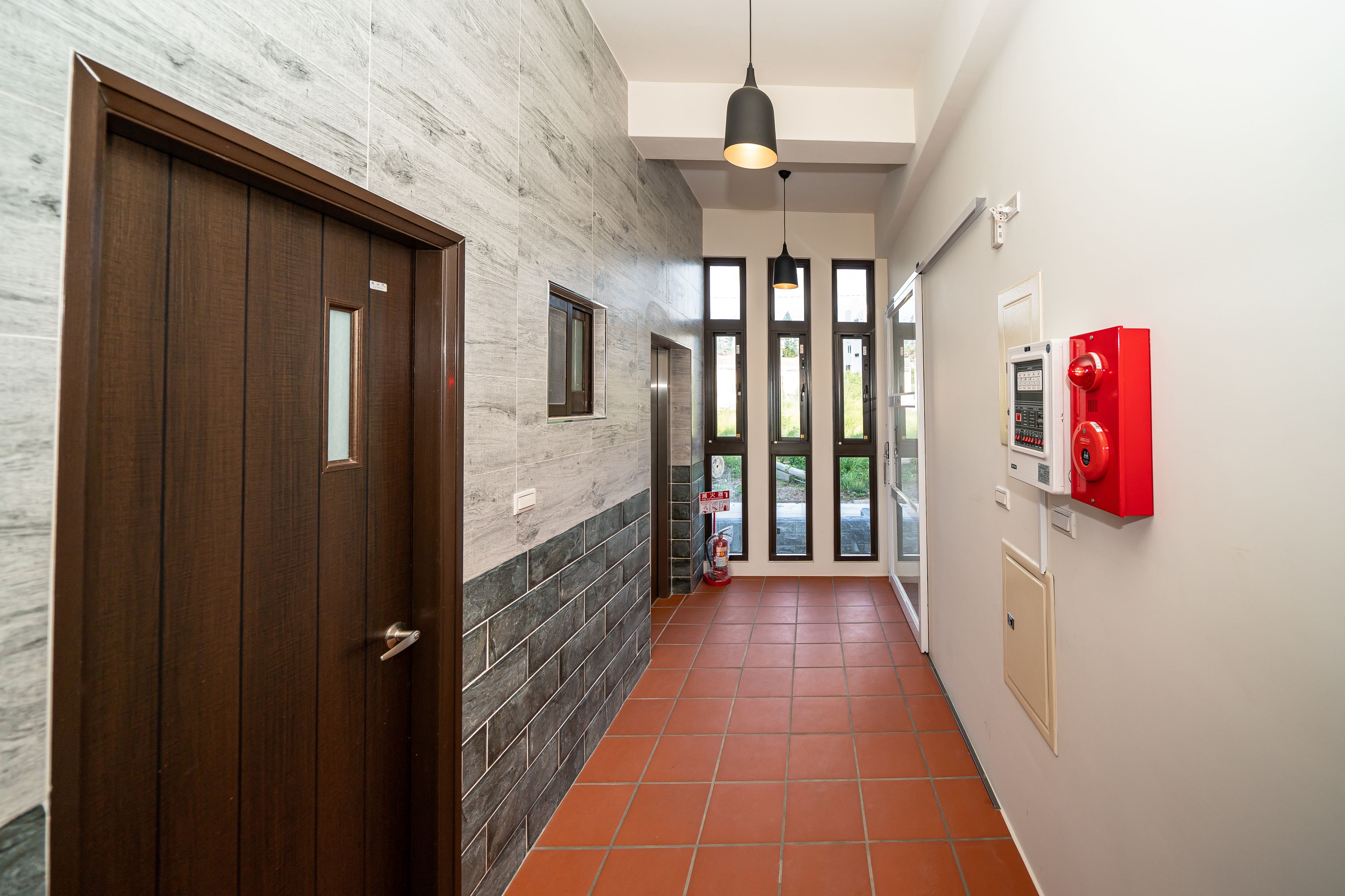 A hallway with a wooden door, a fire alarm, and a red emergency box on the wall.