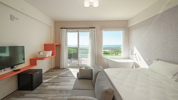 A hotel room with a large bed, a TV, a small desk, and a balcony with a view of the landscape.