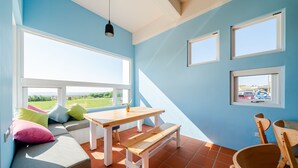 A bright room with a large window, a wooden table, a bench, and a sofa with colorful cushions.
