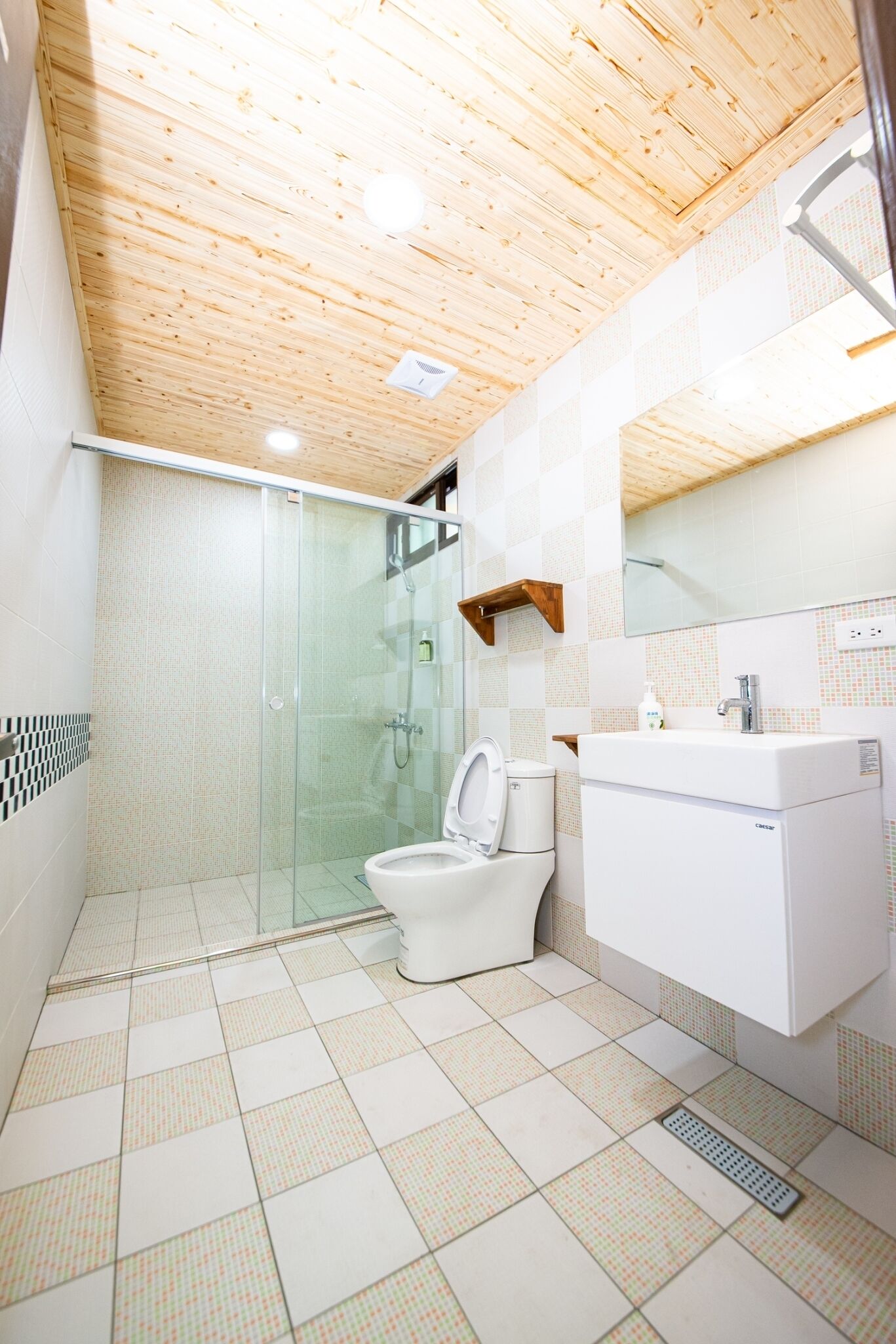 A modern bathroom with a wooden ceiling, a glass shower enclosure, a toilet, and a sink with a mirror above it.