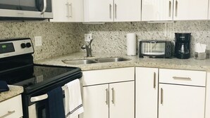 Une cuisine avec des meubles blancs, un four à micro-ondes, un grille-pain, une machine à café et une cuisinière.