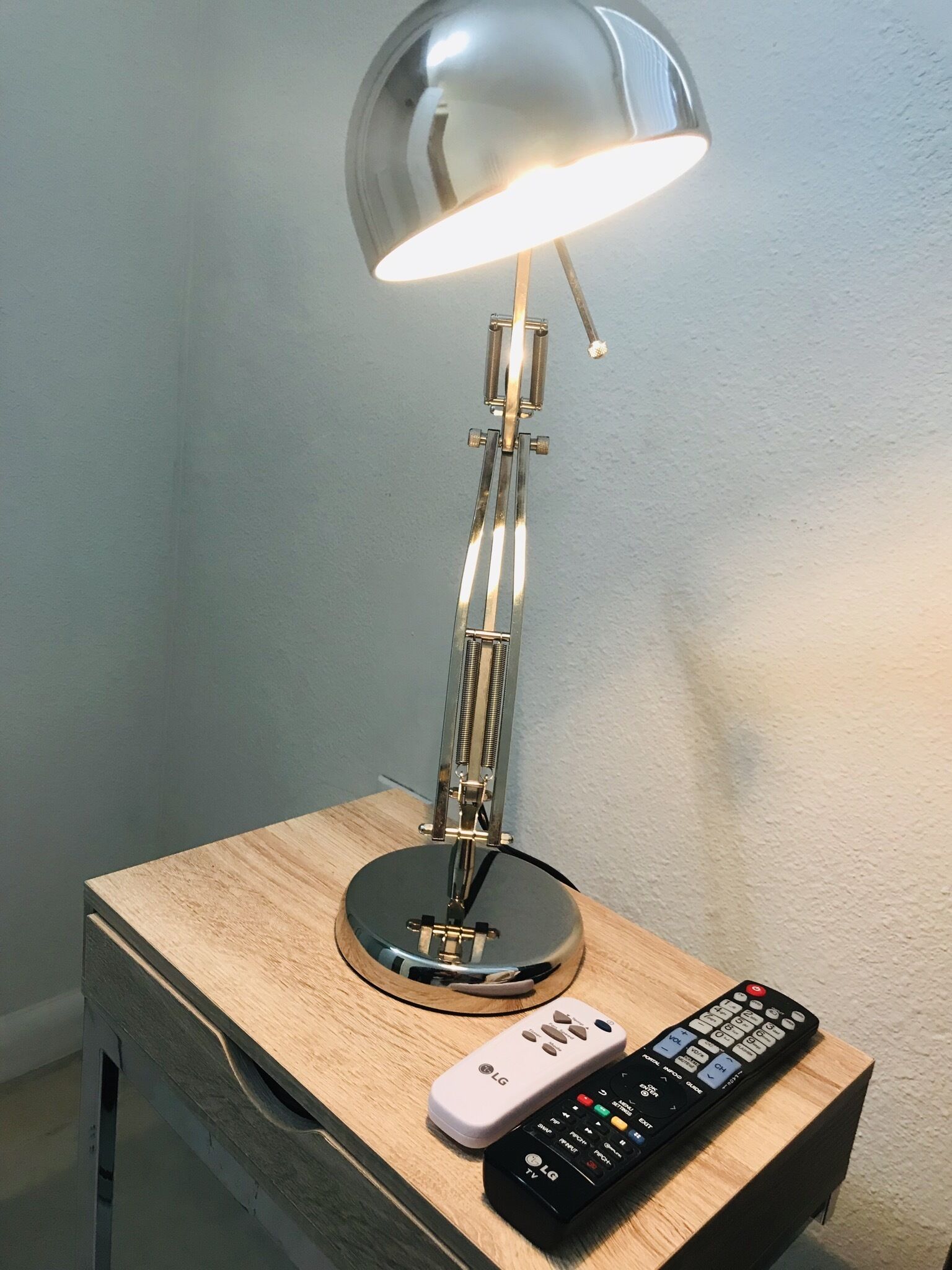 A lamp on a bedside table with a remote control beside it.
