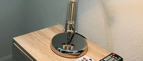 A lamp on a bedside table with a remote control beside it.