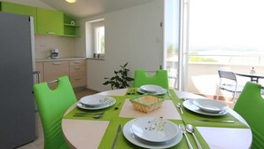Zona pranzo con tavolo apparecchiato per quattro persone, una sedia verde, un frigorifero e una finestra con vista.