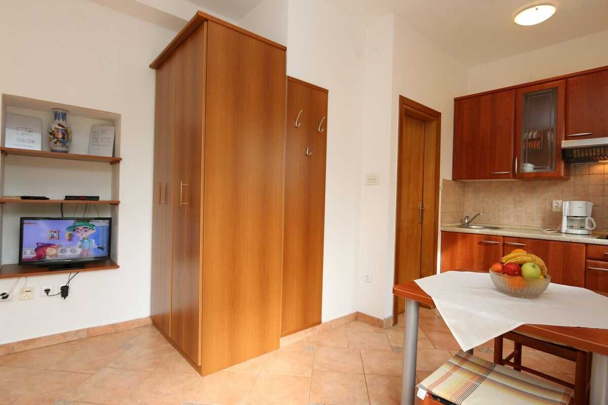 Una cocina con armarios de madera, un televisor en un estante y una mesa con un frutero.