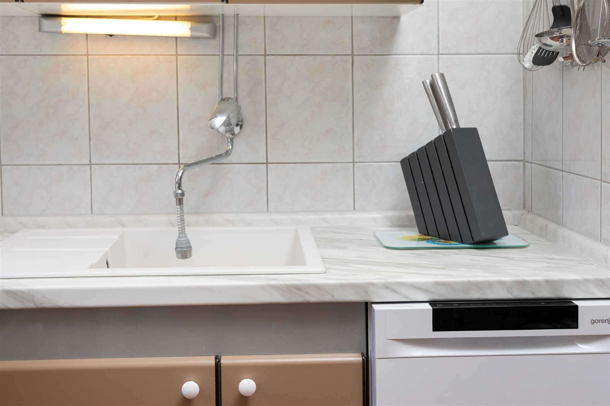 A kitchen with a white countertop, a modern faucet, a black knife block, and a dishwasher.