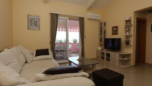 A living room with a sofa, a television, a small table, and a sliding glass door leading to an outdoor area. - Apartment Klimno View Point (Klimno - island Krk)