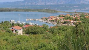 A coastal town with a marina, houses with red roofs, and mountains in the background. - Apartment Klimno View Point (Klimno - island Krk)