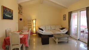 A living room with a sofa, a dining table with chairs, a lamp, and a painting on the wall. - Apartment Klimno View Point (Klimno - island Krk)
