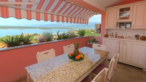 A kitchen with a view of the sea, a dining table with chairs, and a fruit bowl. - Apartment Klimno View Point (Klimno - island Krk)