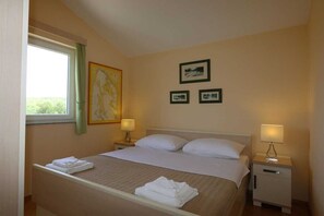 Una habitación de hotel con cama, dos mesitas de noche, una ventana con cortinas y cuadros en la pared.