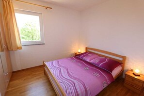 Un dormitorio con cama, lámparas de noche, una ventana con cortinas y suelo de madera.