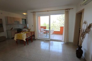Una cocina con armarios, una mesa de comedor con sillas, una puerta corrediza de vidrio a un balcón, y un jarrón con plantas secas.