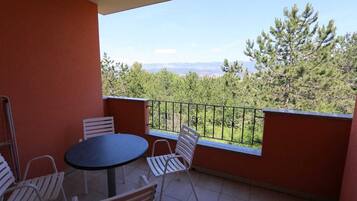 A balcony with a round table and chairs, a view of trees and mountains, and a red wall.