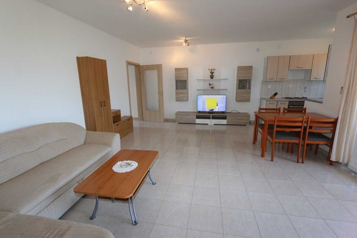 Un salon moderne avec un canapé, une table basse en bois, un téléviseur, un coin repas avec des chaises et, au fond, une cuisine.