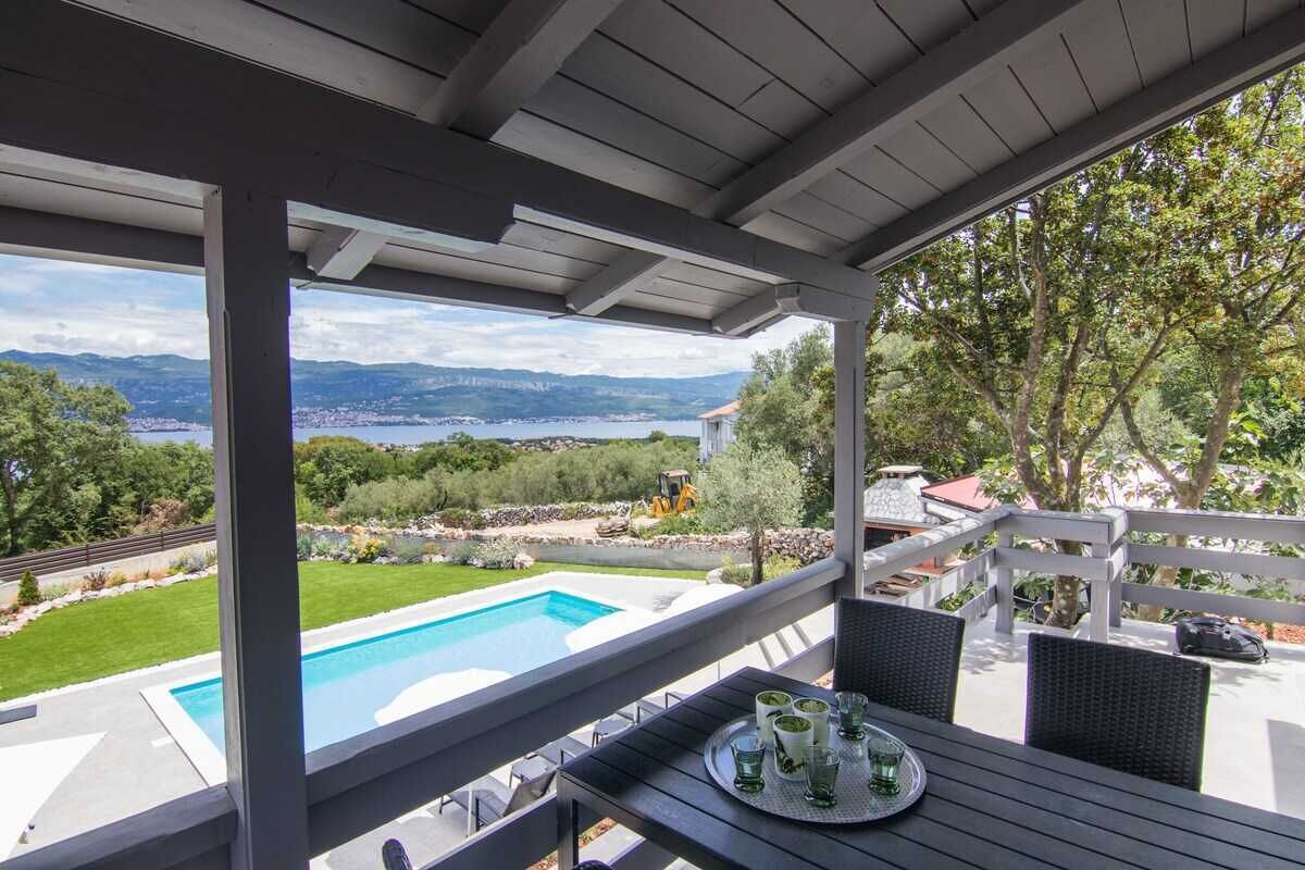 A covered outdoor area with a pool, patio furniture, and a scenic view of mountains and a lake.