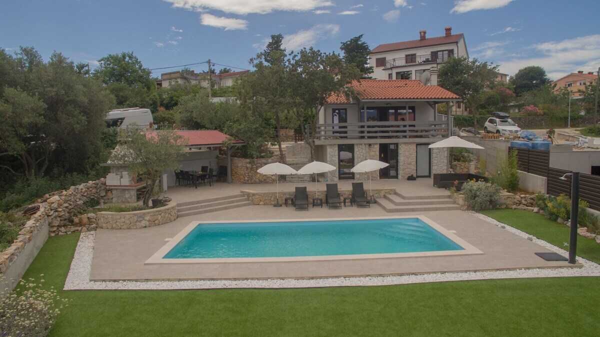 Una piscina con sillones de descanso y sombrillas, rodeada de un césped cuidado y muros de piedra.