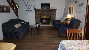 Een woonkamer met een open haard, twee banken, een houten tafel en een televisie boven de open haard.