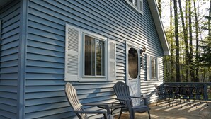 Een blauw huis met een veranda, twee Adirondack-stoelen en een tafel.