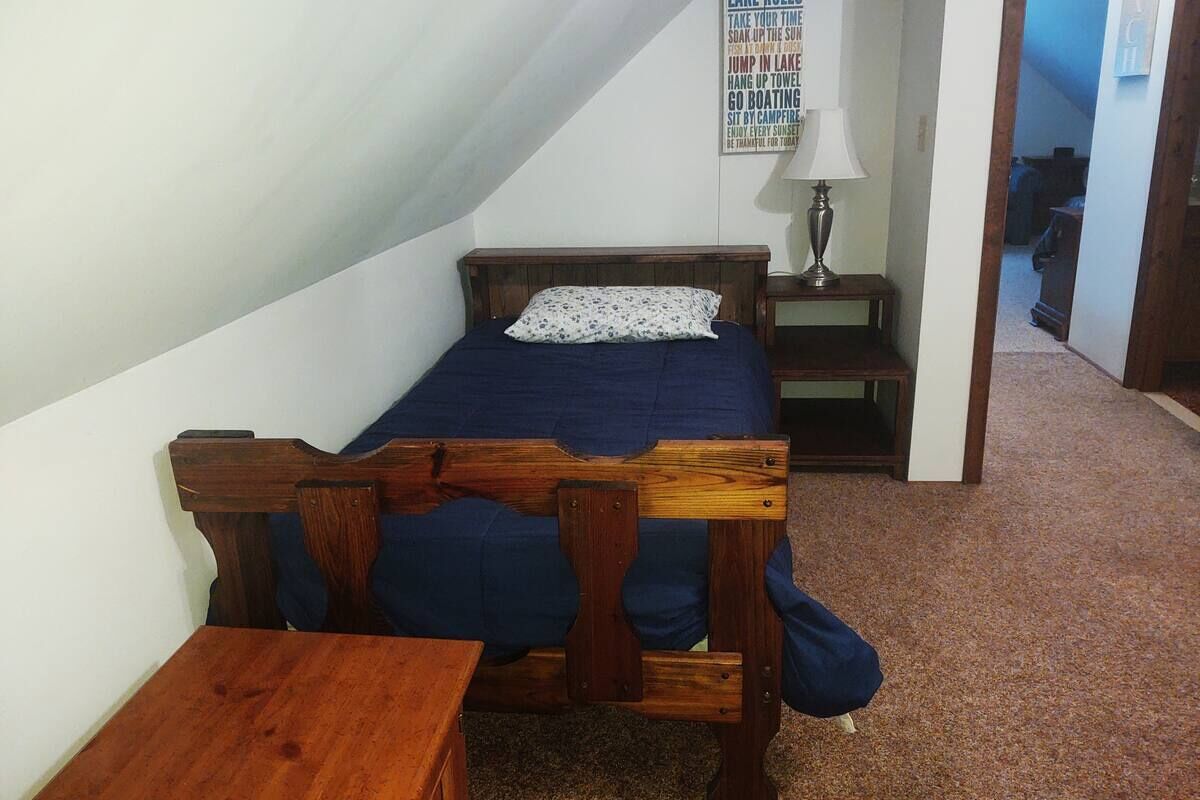 Una habitación pequeña y acogedora con una cama individual, una mesa de madera y una mesita de noche.