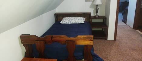Una habitación pequeña y acogedora con una cama individual, una mesa de madera y una mesita de noche.