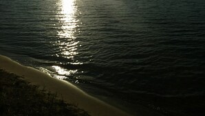 Een strand met een kalme zee, zon die in het water reflecteert, en een heldere lucht.