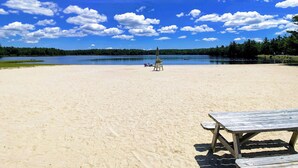 Ein Strand mit einer Holzbank und einem Picknicktisch, umgeben von einem See und einem Wald.