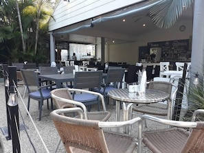 Un área de estar al aire libre con sillas y mesas de mimbre, una zona de bar con un menú y vistas a la calle.