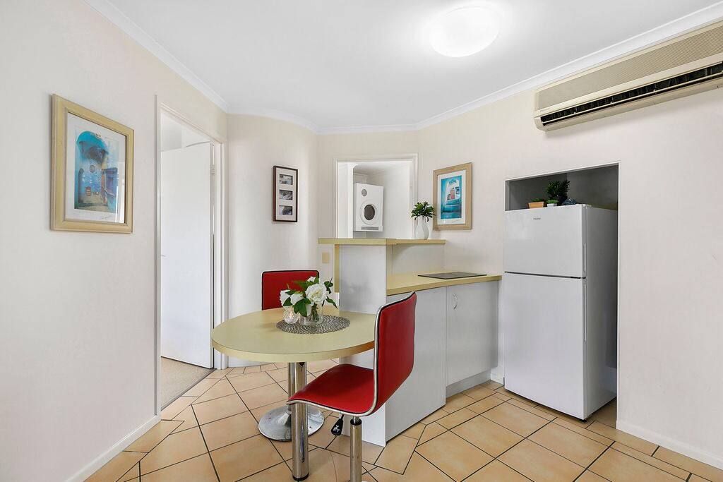 A compact kitchen with a dining table, chairs, a refrigerator, and a small countertop.