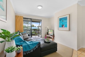 A modern living room with a sofa, a coffee table, a TV, and a balcony with a view. - Gorgeous Apartment in Luxurious Noosa Resort (Noosaville)
