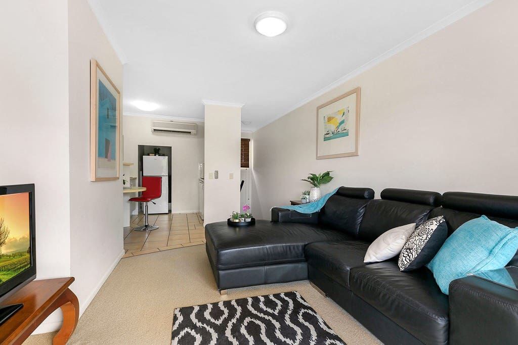 A modern living room with a black leather sofa, a flat-screen TV, and a patterned rug.