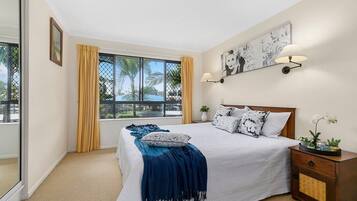 A bedroom with a large bed, a nightstand, a wall-mounted lamp, and a window with curtains.