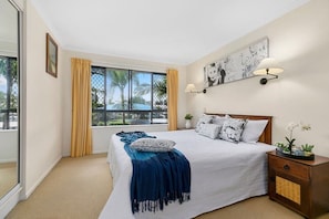 A bedroom with a large bed, a nightstand, a wall-mounted lamp, and a window with curtains.