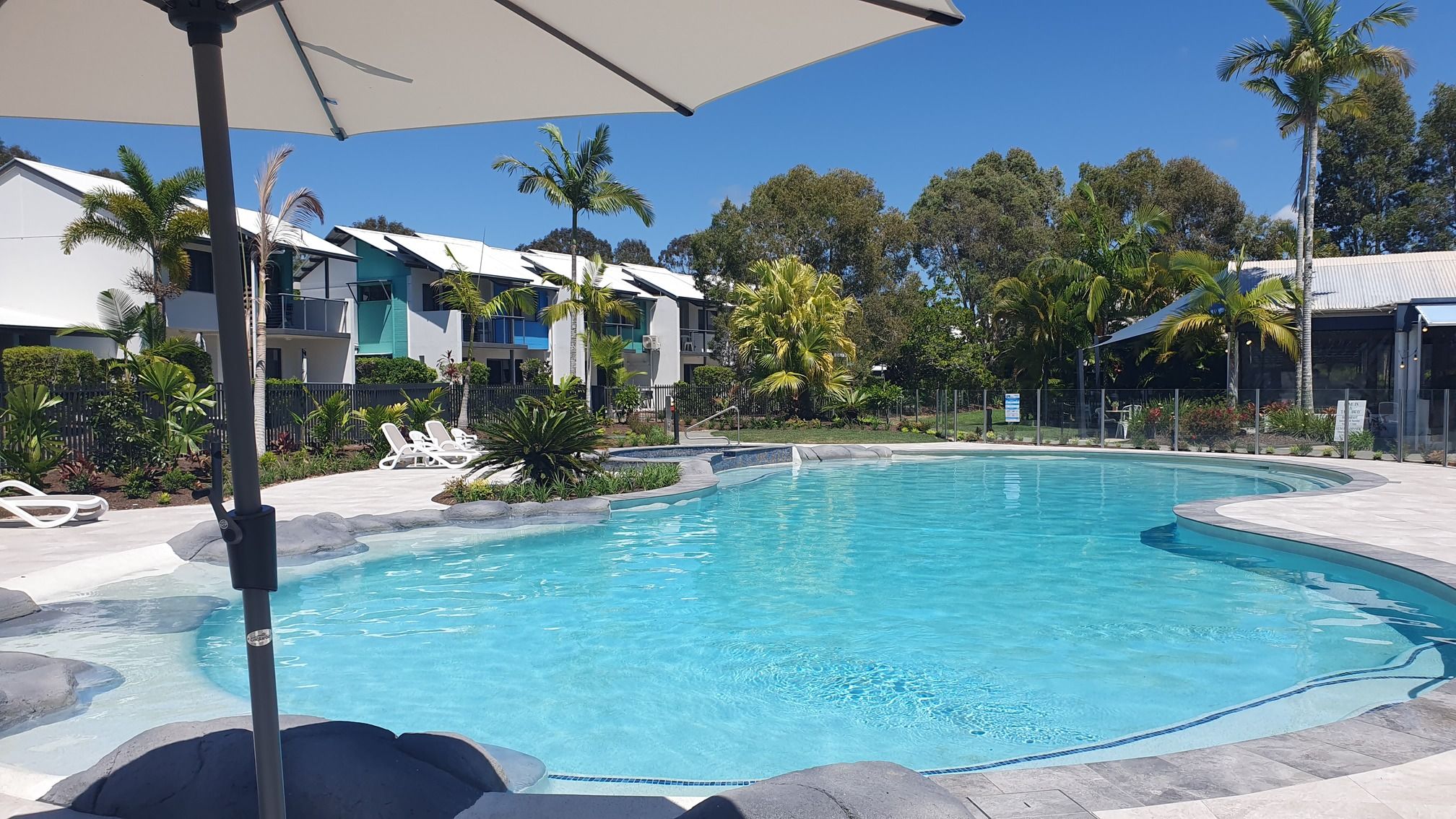 A swimming pool with lounge chairs and a covered area, surrounded by greenery and buildings.