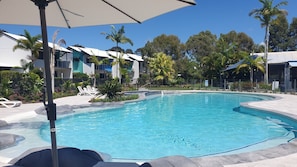 A swimming pool with lounge chairs and a covered area, surrounded by greenery and buildings. - Gorgeous Apartment in Luxurious Noosa Resort (Noosaville)