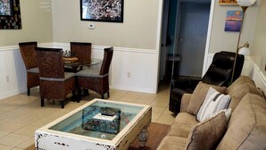 Ein Wohnzimmer mit Glastisch, braunem Ledersofa und einem Essbereich mit Korbstühlen.