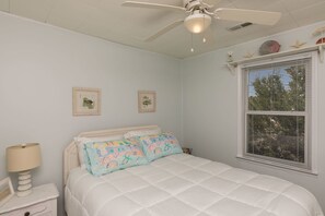 A bedroom with a bed, a ceiling fan, a window with blinds, and wall-mounted starfish decorations. - South Shore Beach Haven - 3 bedroom, 2nd Row Cottage! Dog Friendly! (Surf City)