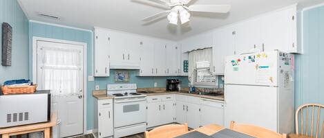 A compact kitchen with white cabinets, a stove, a refrigerator, and a ceiling fan.