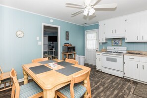 A compact kitchen with white cabinets, a microwave, and a stove. There is a dining table with chairs and a ceiling fan above. - South Shore Beach Haven - 3 bedroom, 2nd Row Cottage! Dog Friendly! (Surf City)