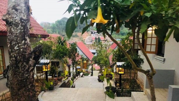 A pathway leading to a building with red roofs, surrounded by potted plants and trees.