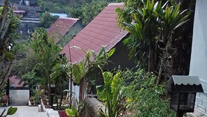 A pathway leading to a row of houses with red roofs, surrounded by lush greenery and a clear sky.